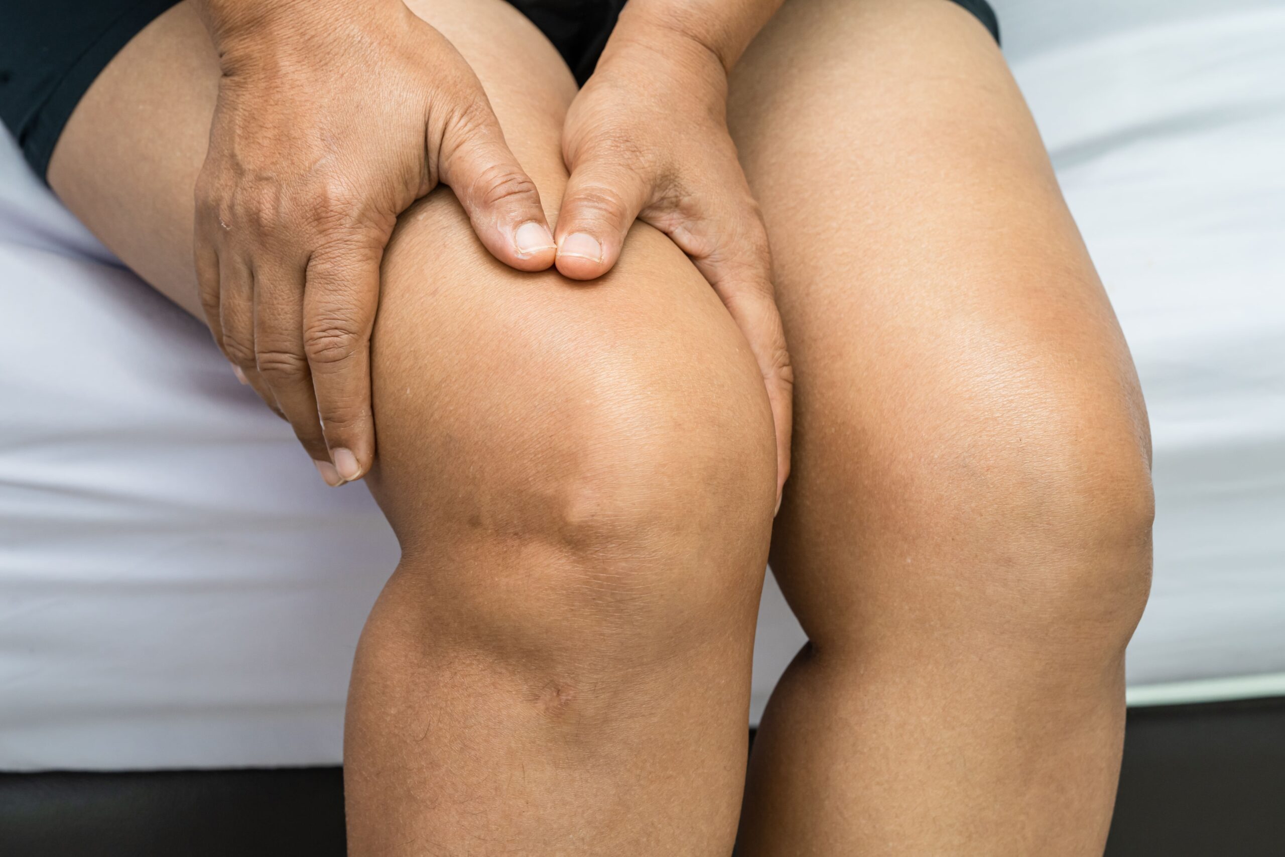 A person is sitting with their hands resting on their knees, appearing to be in discomfort.