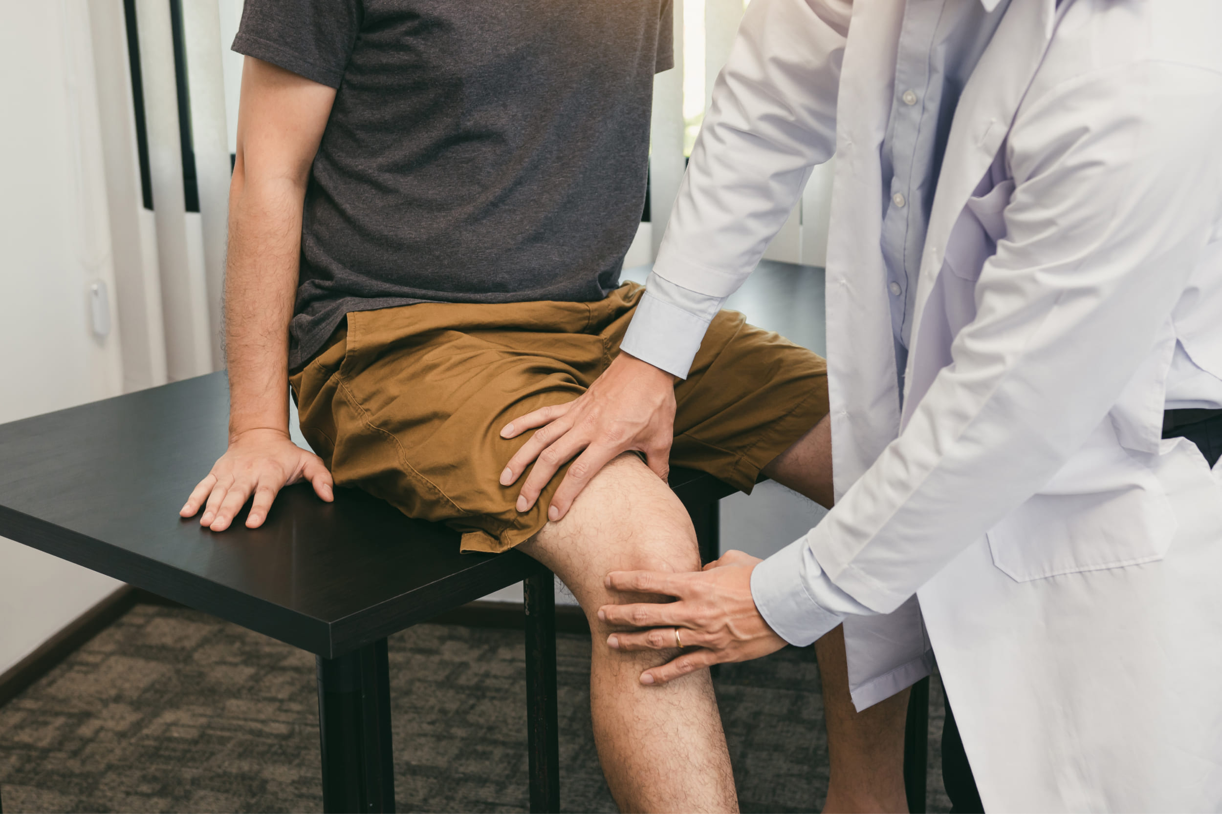 A healthcare professional examines the knee of a seated patient during a medical consultation.