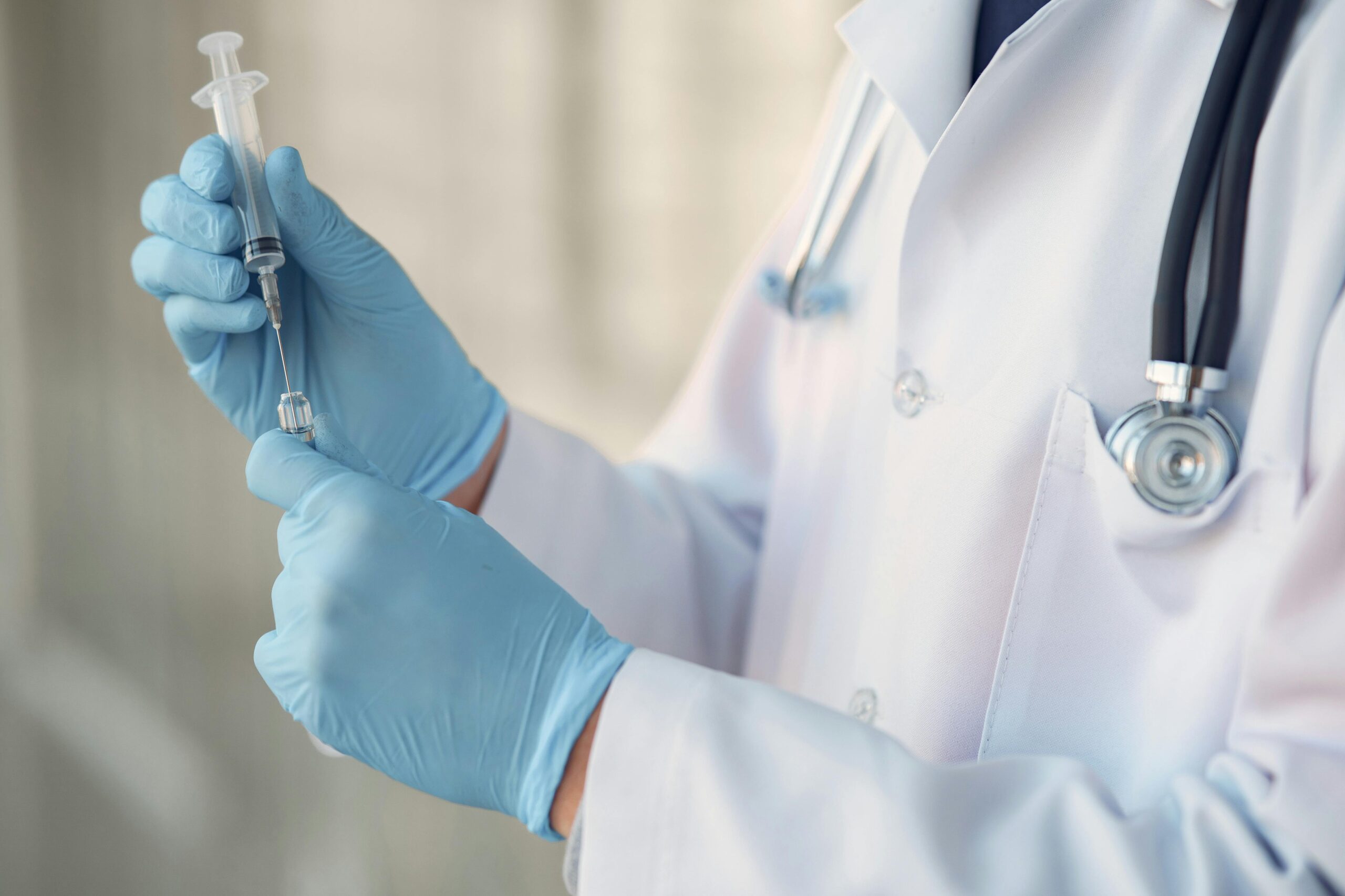 A healthcare professional in blue gloves prepares a syringe for vaccination.