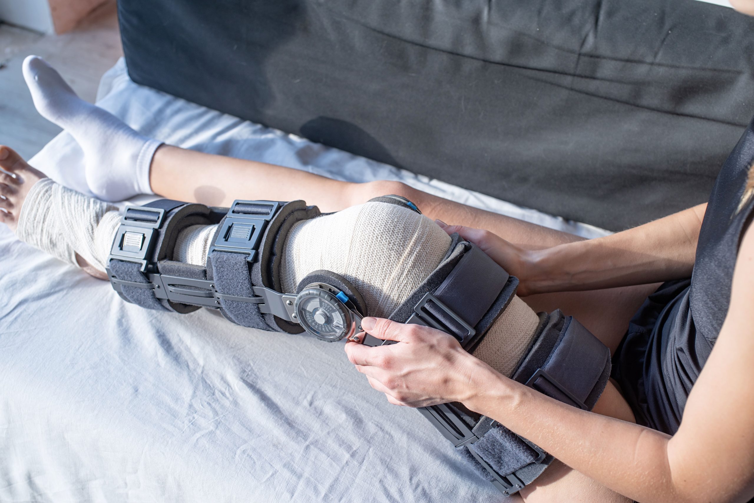 A person adjusting a knee brace while sitting on a couch at home.